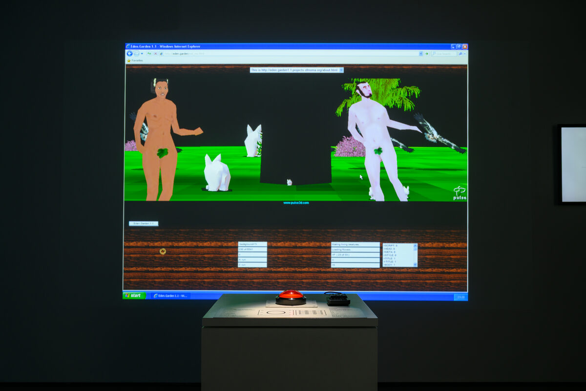 Eden.Garden in the exhibition: the restored work projected large in a dark room — its 3D paradise scene inside a period Internet Explorer window — with a podium carrying a single red trackball button in front.