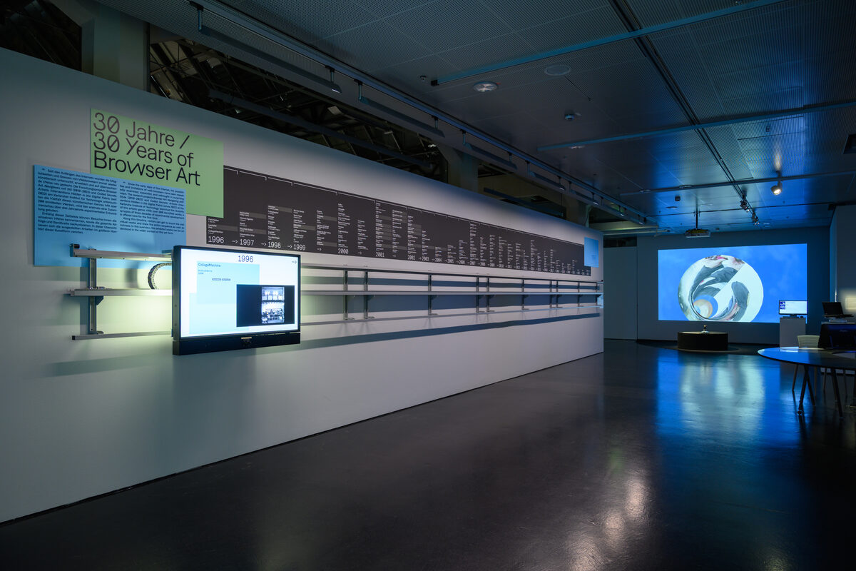 Exhibition view: a long gallery wall carrying the printed timeline '30 Jahre / 30 Years of Browser Art', with a monitor station mounted on it and a large projection in the darkened room beyond.